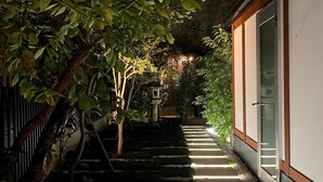 A nighttime outdoor pathway with steps leading to a building, surrounded by greenery and a stone lantern.
