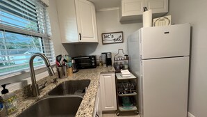 A kitchen with a double sink, a toaster, a refrigerator, and a window with blinds.