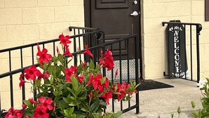 A building entrance with a black door, a welcome sign, and red flowers in the foreground.