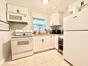 A kitchen with white cabinets, a stove, a microwave, a coffee maker, and a refrigerator.