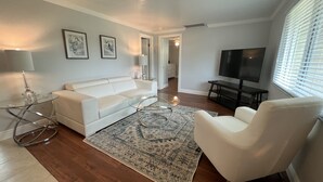 A modern living room with a white sofa, glass coffee table, and a patterned rug.