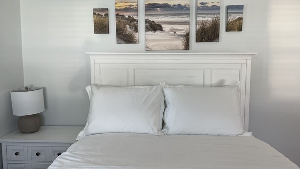 A bedroom with a white bed, a nightstand with a lamp, and three framed pictures on the wall.
