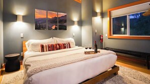 A bedroom with a bed, wall-mounted lights, a window with blinds, and a fireplace.
