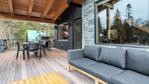 A covered outdoor area with a wooden deck, a gray sofa, and a table.