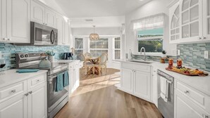 A modern kitchen with white cabinetry, a central island, and a dining area with a chandelier.