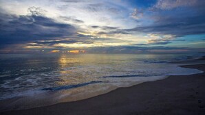 A beach with waves, a clear sky, and a sunset.