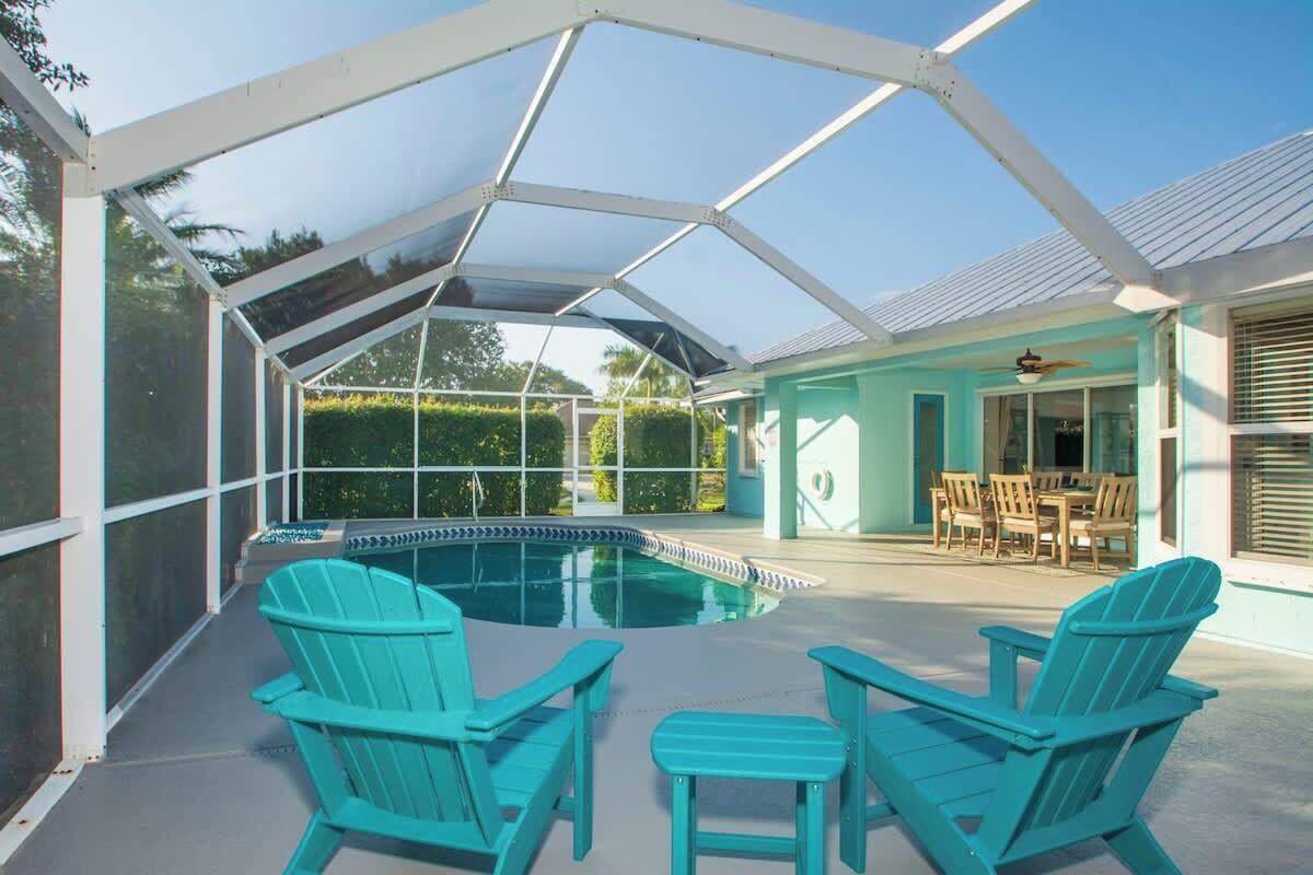 A covered outdoor swimming pool with chairs, a dining area, and a building with a light blue exterior.