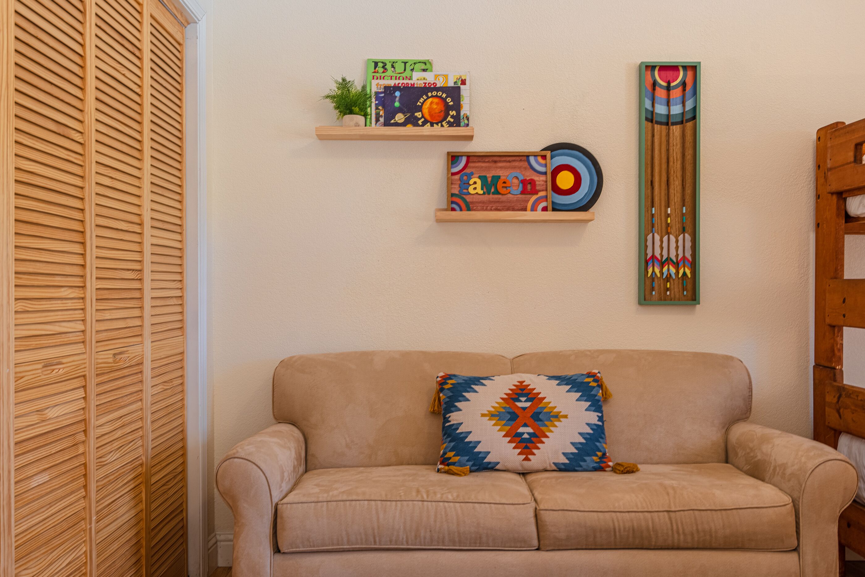 Un sofá beige con un cojín colorido, un armario con puertas de listones de madera y adornos en la pared.