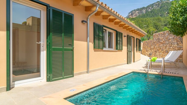 Ein Schwimmbad neben einem Gebäude mit grünen Fensterläden und einer Steinmauer.