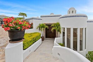 A white building with a blue decorative border, a wooden door, and a potted plant with red flowers.