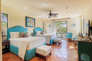 A hotel room with two beds, a ceiling fan, artwork on the walls, and a view of palm trees through the window. - Condo B305 - 2 Bdrm Luxury Condo with Ocean Views (Cabo San Lucas)