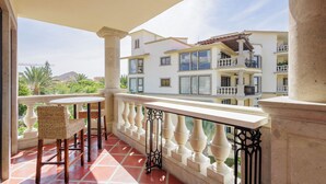 Un balcon donnant sur un immeuble à plusieurs étages, avec des chaises en osier et un sol carrelé.