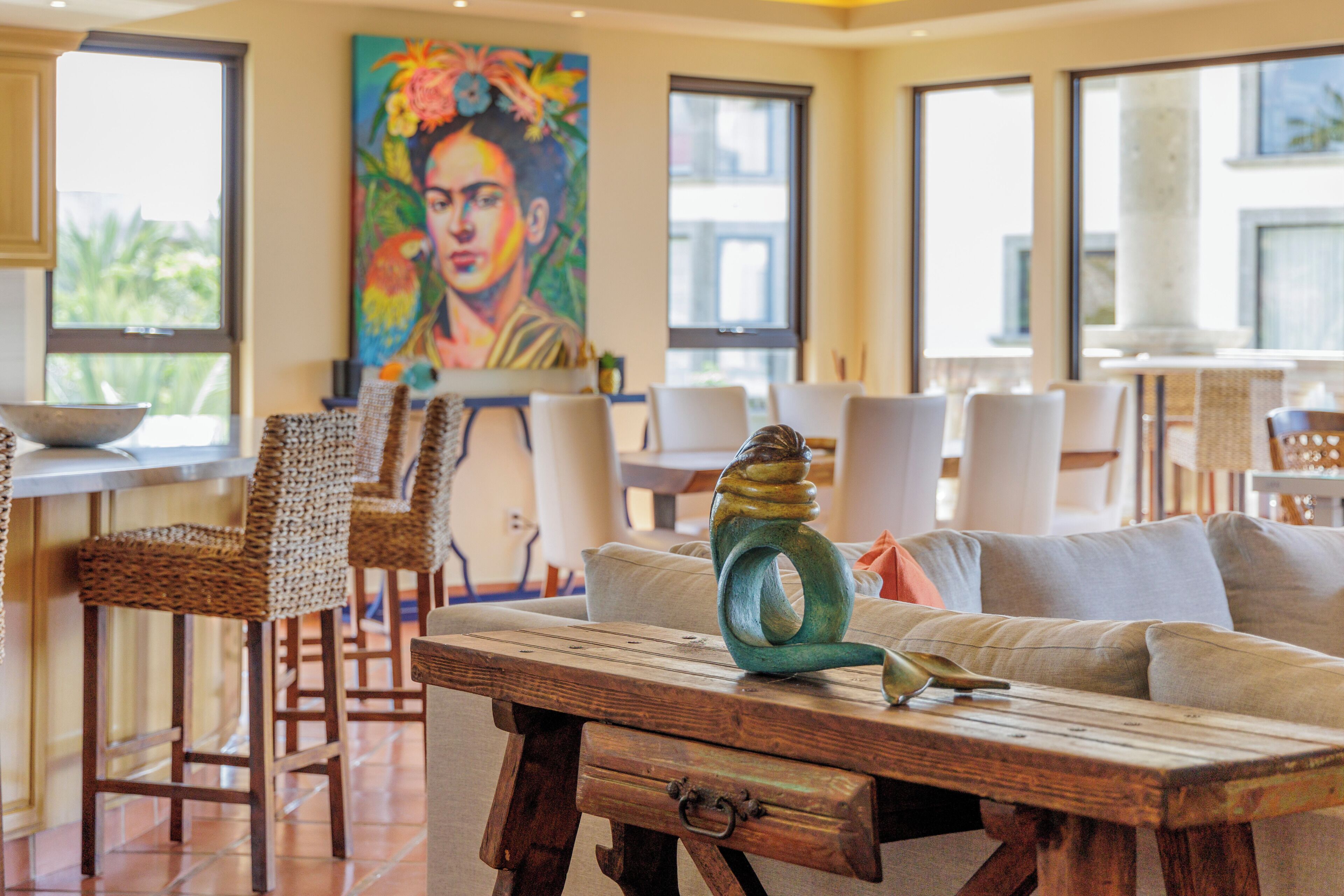 A dining area with wicker chairs, a wooden table, and a colorful painting on the wall.