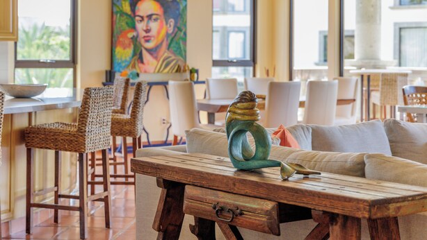 Un coin repas avec des chaises en osier, une table en bois et un tableau coloré accroché au mur.