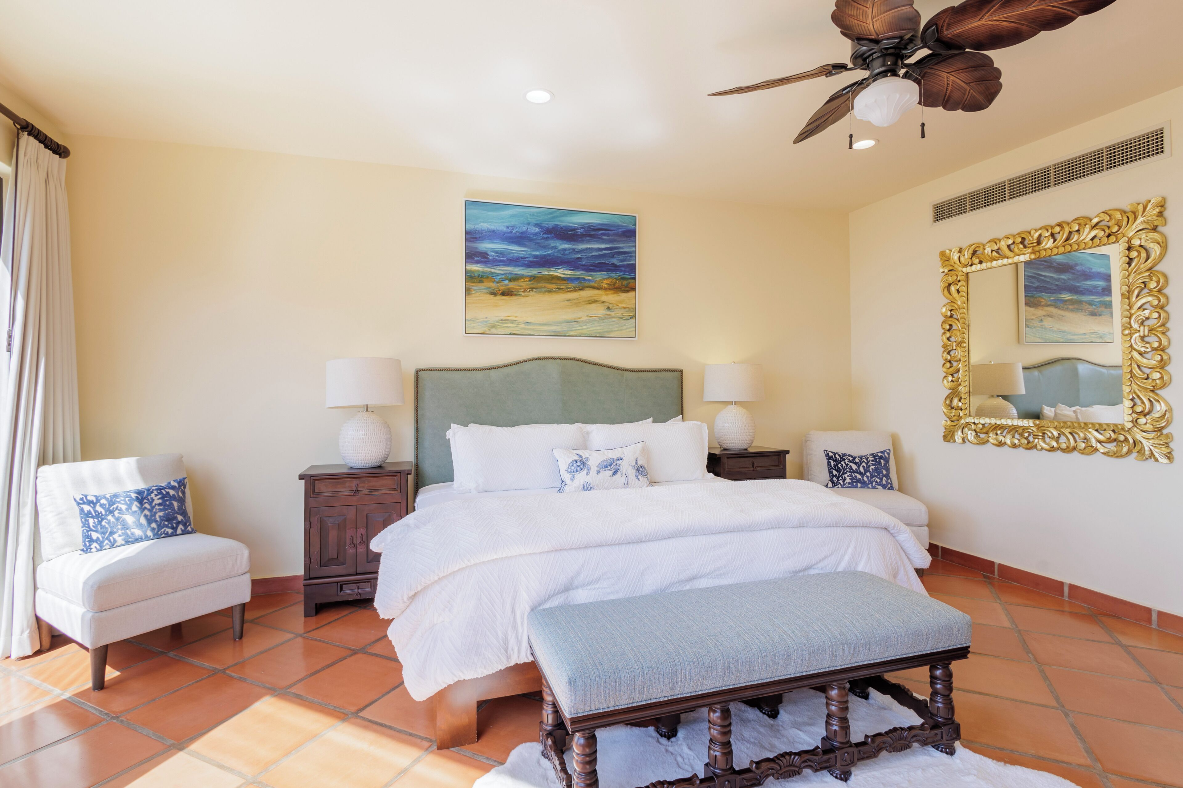 A bedroom with a bed, two bedside tables, a chair, a ceiling fan, and a painting on the wall.