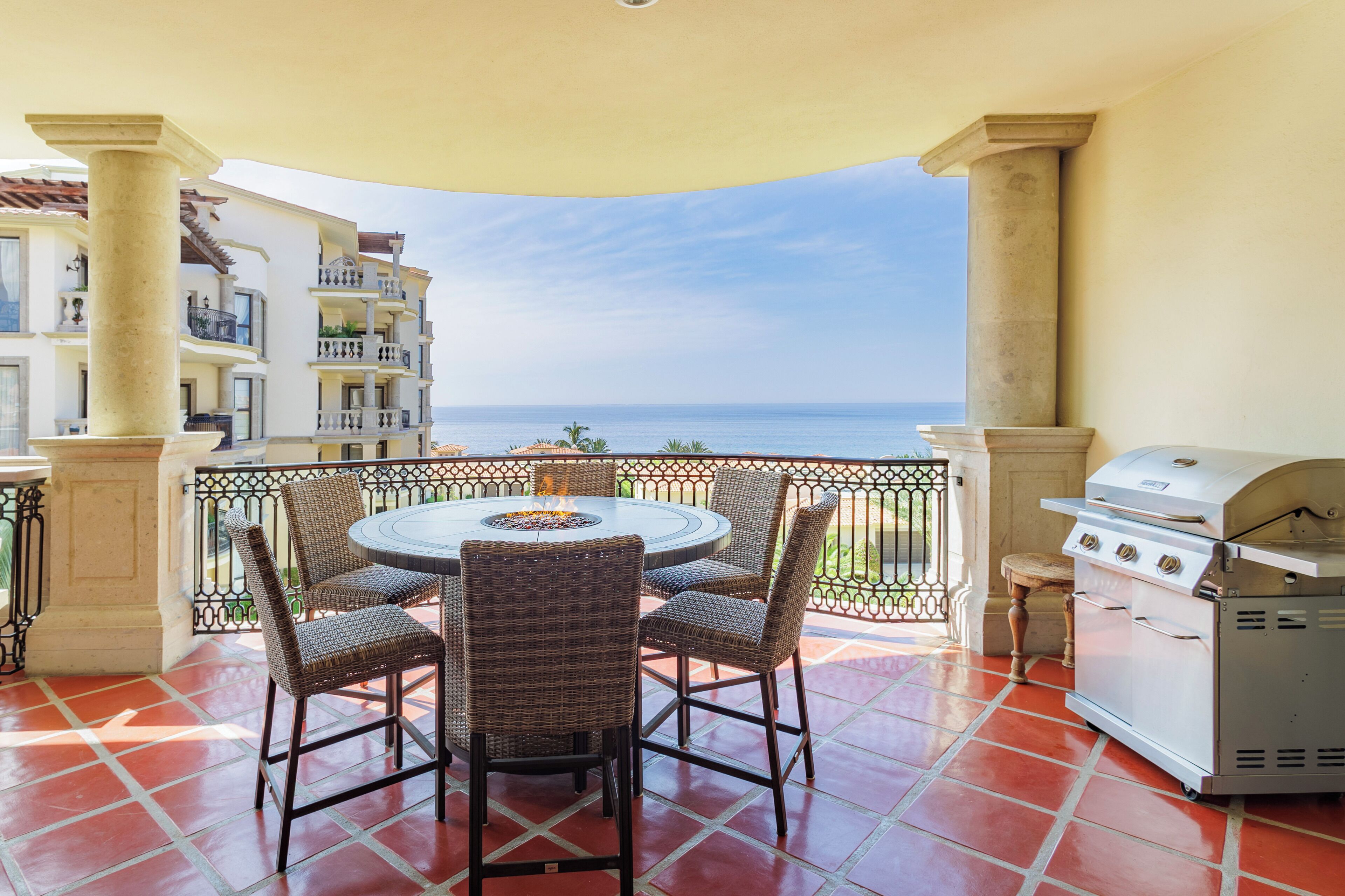 Eine Terrasse mit rundem Tisch und Stühlen, einem Grill und Blick auf das Meer.