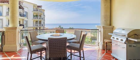 Eine Terrasse mit rundem Tisch und Stühlen, einem Grill und Blick auf das Meer.