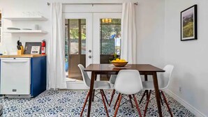 Un coin repas avec une table, des chaises et un saladier rempli de fruits. On y trouve également un réfrigérateur blanc et un meuble bleu.