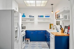 A compact kitchen with white and blue cabinetry, a small stool, and a patterned floor.