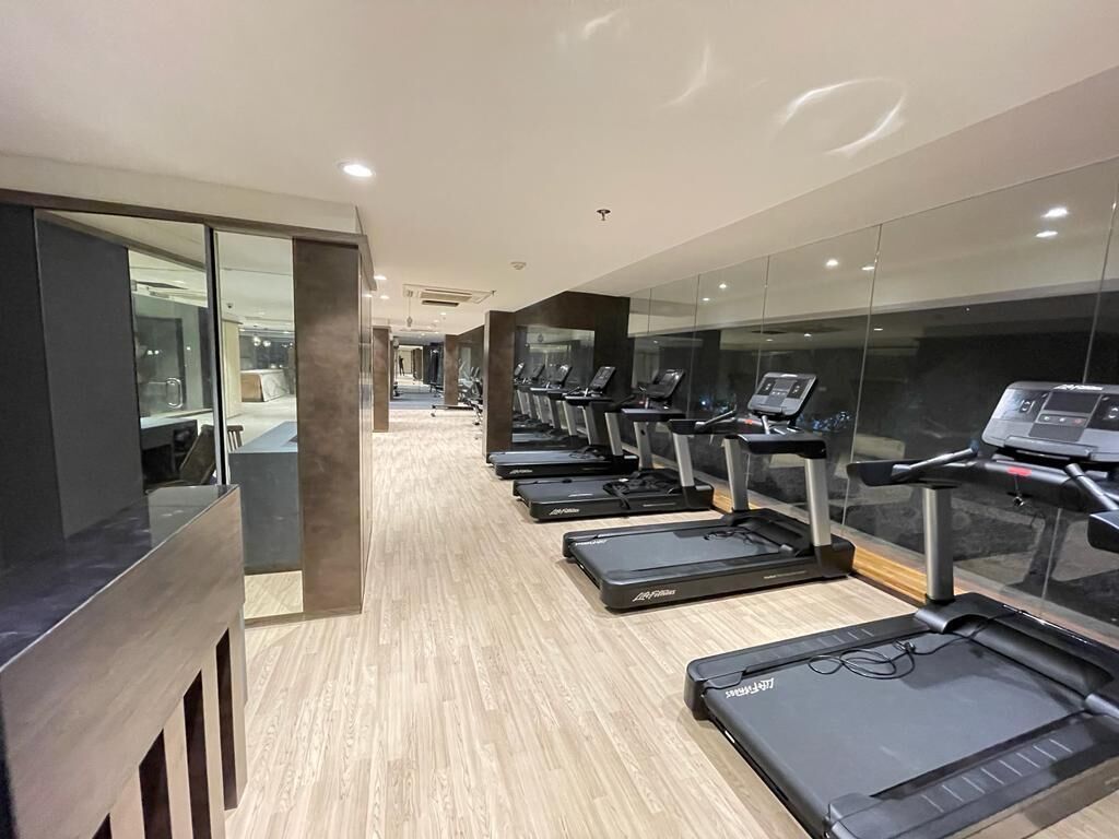 A gym with multiple treadmills aligned in a row, a wooden floor, and glass walls.
