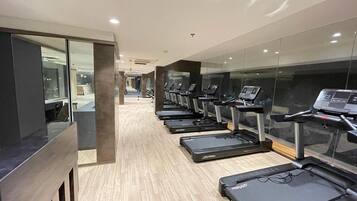 A gym with multiple treadmills aligned in a row, a wooden floor, and glass walls.