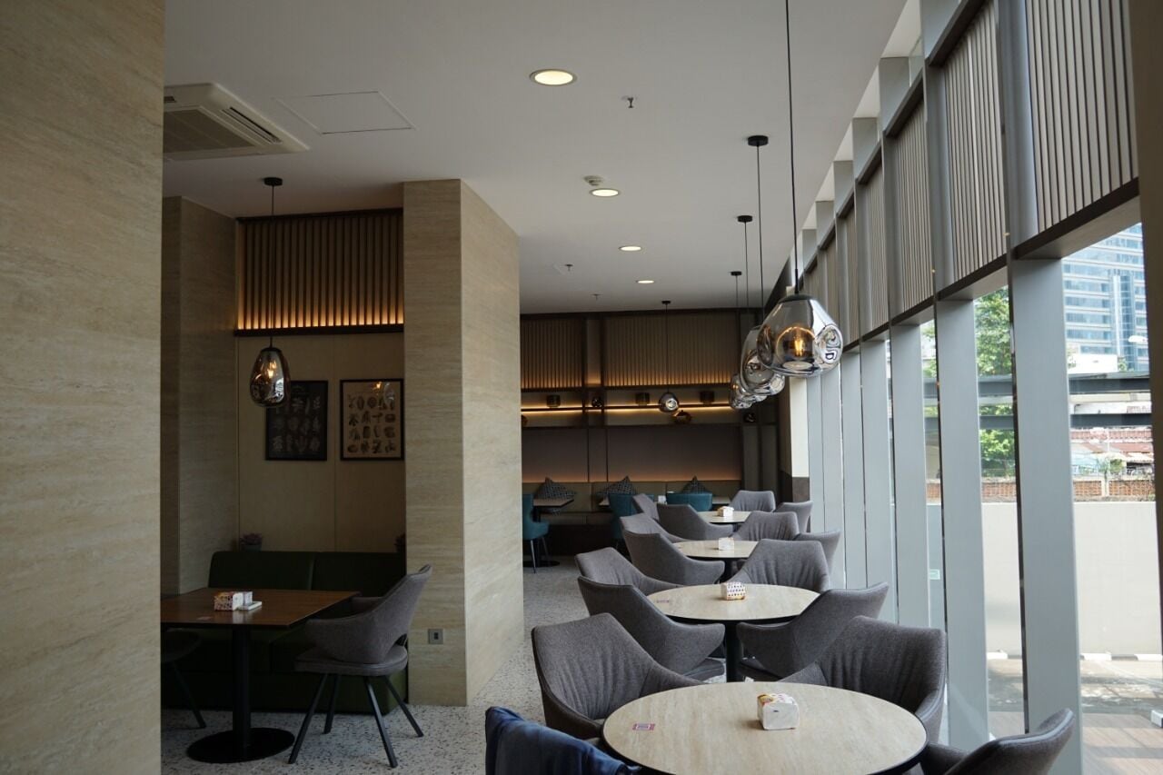 A modern cafe with round tables and grey chairs, large windows, and a wooden ceiling.