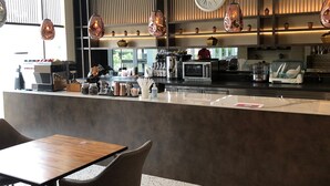 A modern cafe with a wooden counter, hanging pendant lights, and a large wall clock. - The Day Residence (Jakarta)
