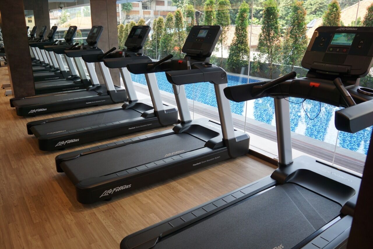 Une rangée de tapis de course dans une salle de sport, avec vue sur une piscine.