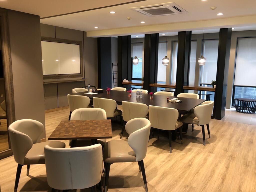 A modern conference room with a large screen, multiple tables, and chairs.