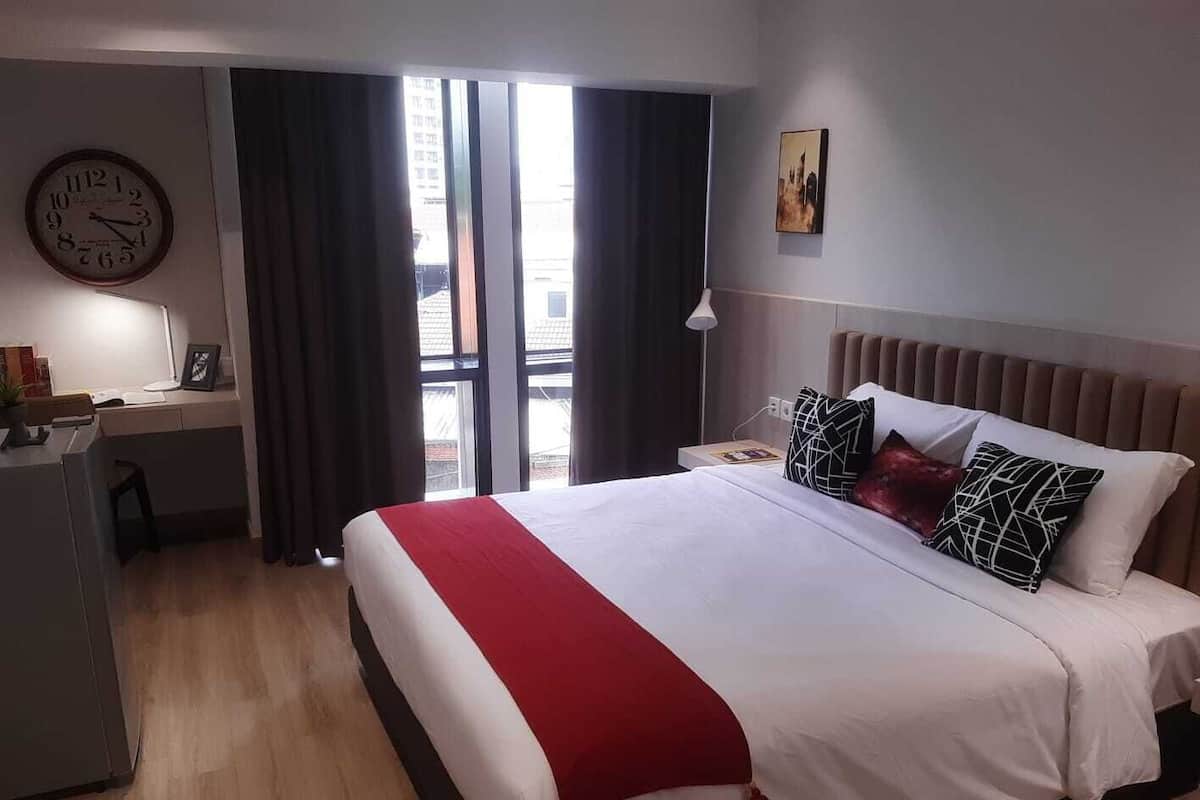 A hotel room with a bed, a desk, a chair, a clock, and a window with curtains.