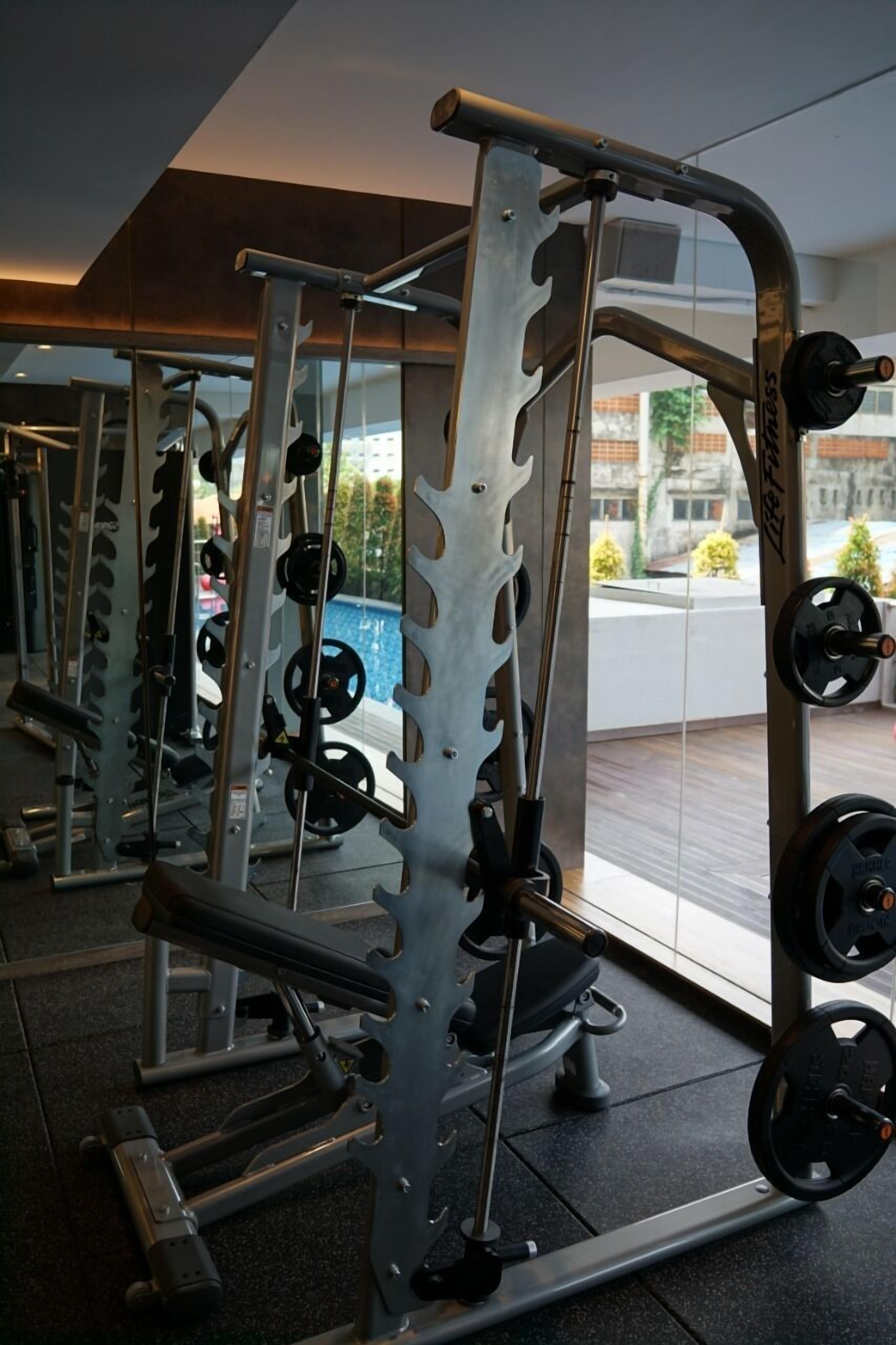 Un gimnasio con equipo de levantamiento de pesas, que incluye una jaula para sentadillas y bancos.