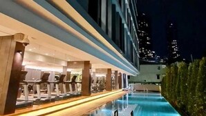 A modern hotel with a swimming pool, a bar area, and a view of the city skyline at night. - The Day Residence (Jakarta)
