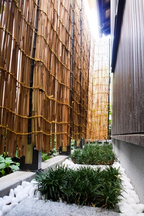 A bamboo fence, white pebbles, and green plants in a garden setting.
