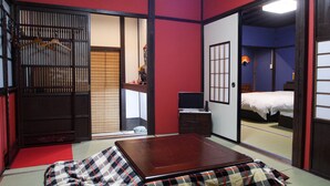 A traditional Japanese room with tatami flooring, a low wooden bed, a television, and a sliding door leading to another room.