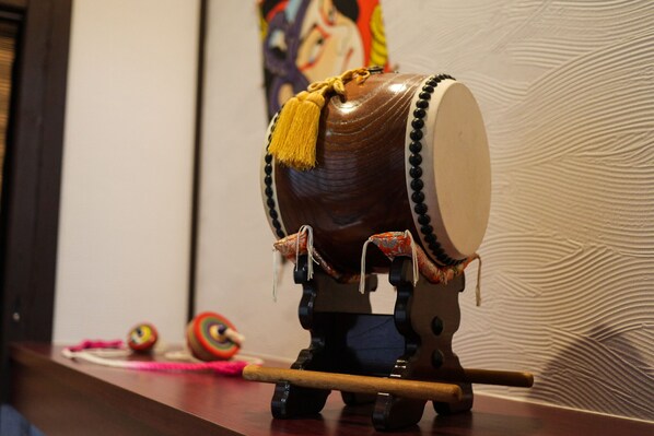 A drum with tassels and a stick, placed on a wooden surface with a patterned wall in the background.