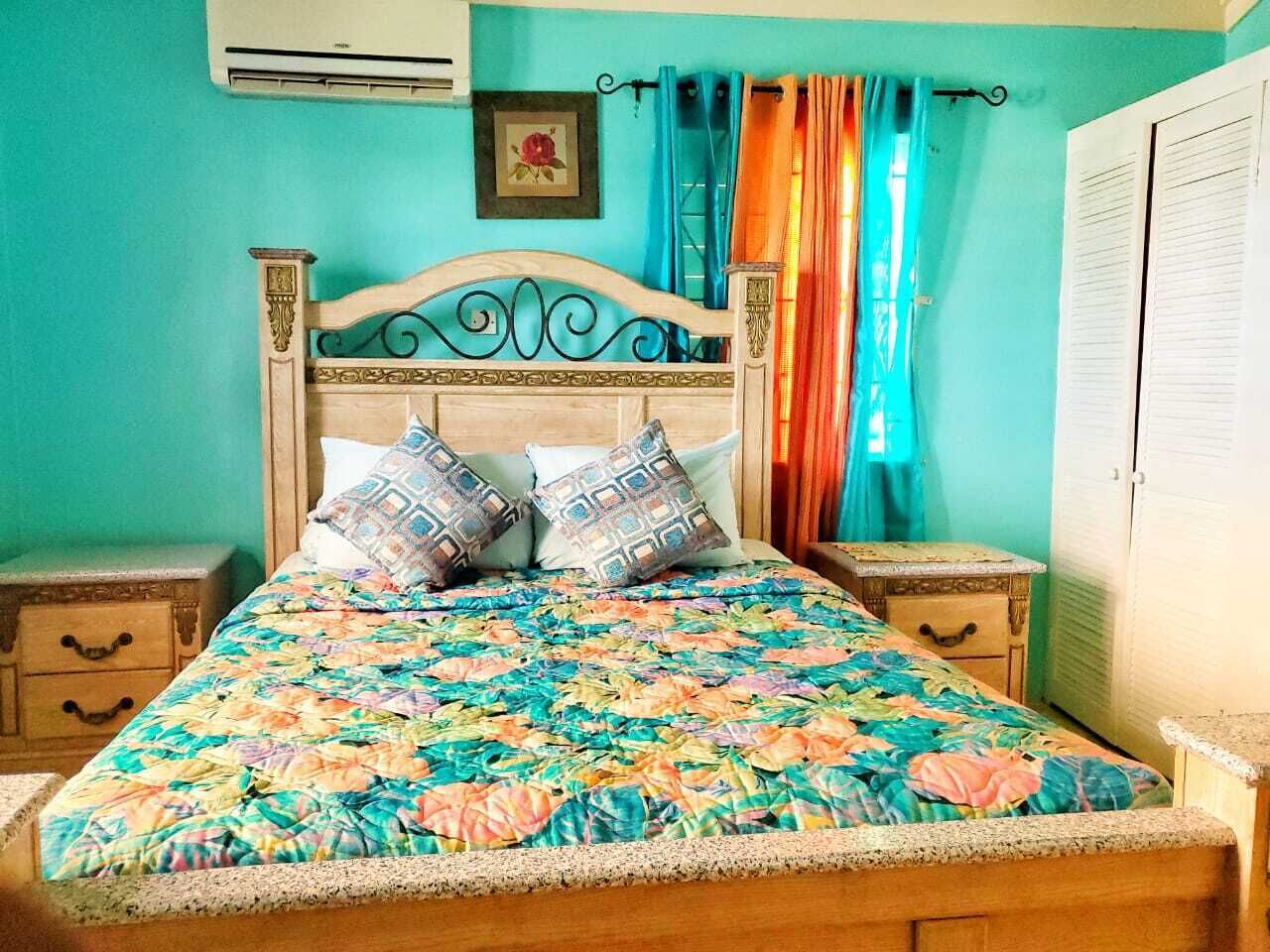 A bed with a floral bedspread, two pillows, and a headboard with decorative carvings. There are two bedside tables, one with a drawer and the other with a small cabinet.