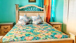 A bed with a floral bedspread, two pillows, and a headboard with decorative carvings. There are two bedside tables, one with a drawer and the other with a small cabinet. - 2 Bed-Sleeps 4-Gated community-5 Min Town Centre (Florence Hall Village)