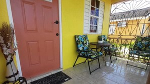 A yellow building with a red door, a small patio with two chairs and a table, and a window with shutters. - 2 Bed-Sleeps 4-Gated community-5 Min Town Centre (Florence Hall Village)