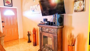 A living room with a fireplace, a television on a stand, and two vases with dried plants. - 2 Bed-Sleeps 4-Gated community-5 Min Town Centre (Florence Hall Village)