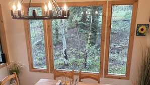 Un tavolo da pranzo in legno con sei sedie, un lampadario e ampie finestre con vista sulla foresta.