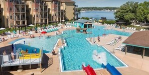 A swimming pool with slides and lounge chairs, surrounded by a building with multiple balconies.