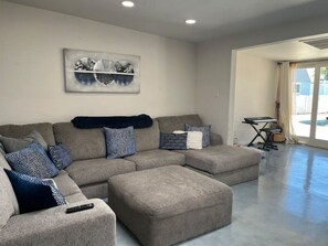 A modern living room with a sectional sofa, ottoman, and a large abstract painting on the wall. - The Oasis- House with pool/ 2 master suites/ fire pit/ outdoor bar (Tucson)