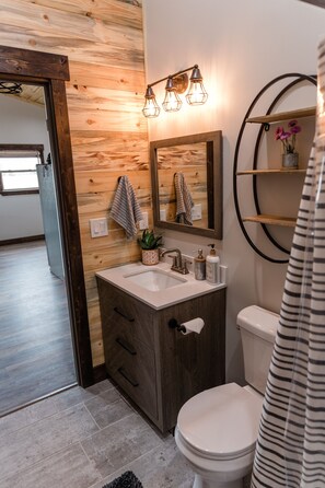 Un baño con pared de madera, un lavamanos blanco, un espejo, un inodoro y una cortina de ducha.