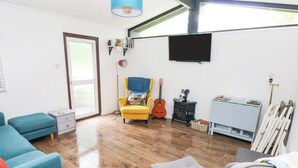 Una sala moderna con suelo de madera, un sillón amarillo, un sillón gris, un sofá azul, una guitarra, un televisor y un radiador.