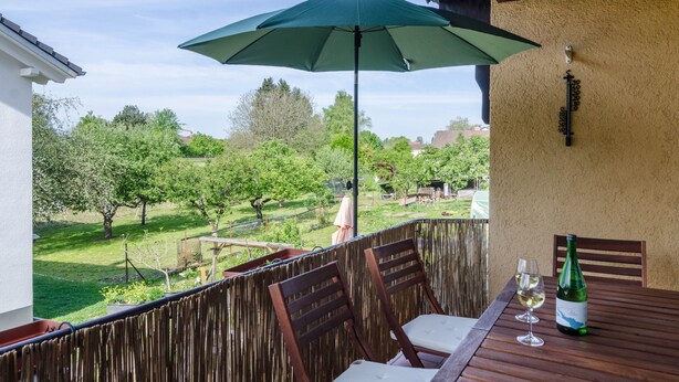 Un balcon avec une table, deux chaises, un parasol vert et une bouteille de vin.