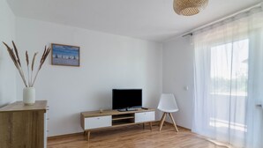 Un salon moderne avec un meuble de rangement en bois, un téléviseur à écran plat, un fauteuil blanc et un tableau accroché au mur.