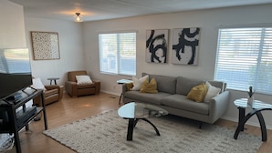 A living room with a sofa, armchair, coffee table, TV, and artwork on the walls.
