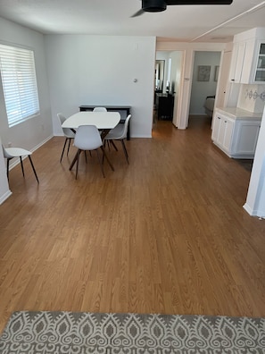 Uma sala de jantar com mesa e cadeiras brancas, piso de madeira e tapete estampado.
