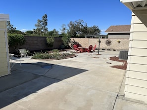 A concrete patio with red chairs and a table, surrounded by a brick wall and greenery.