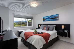 A modern bedroom with a large bed, a desk with a computer, a window with a view, and a painting on the wall.